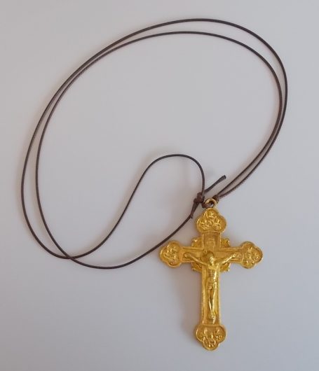 Goldener Kreuzanhänger an einer braunen Kette.