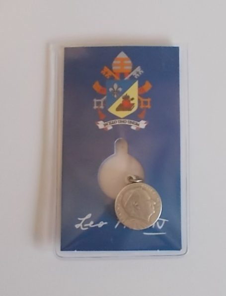 Papstmedaille auf blauem Hintergrund in Schutzhülle mit Unterschrift.